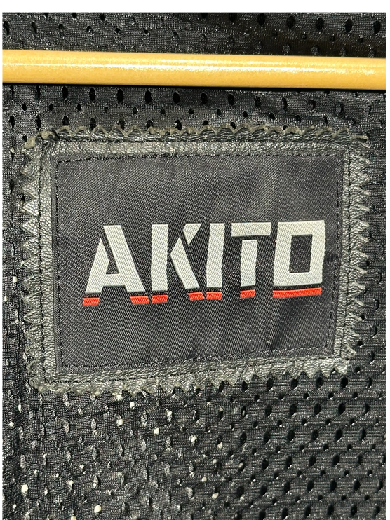 Close-up of the AKITO brand logo patch stitched onto the black breathable mesh interior lining of an OutOf10 jacket.