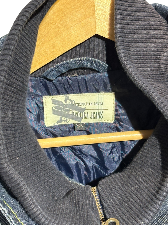 OutOf10 bomber jacket interior featuring a blue quilted lining, ribbed collar, and Metropolitan Denim brand label.