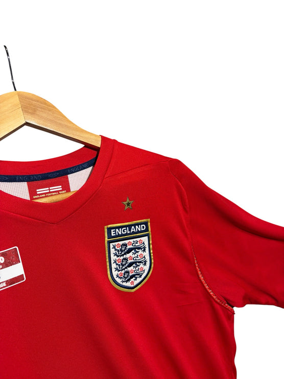 OutOf10 red England national football team jersey with crest and gold star detail on a wooden hanger