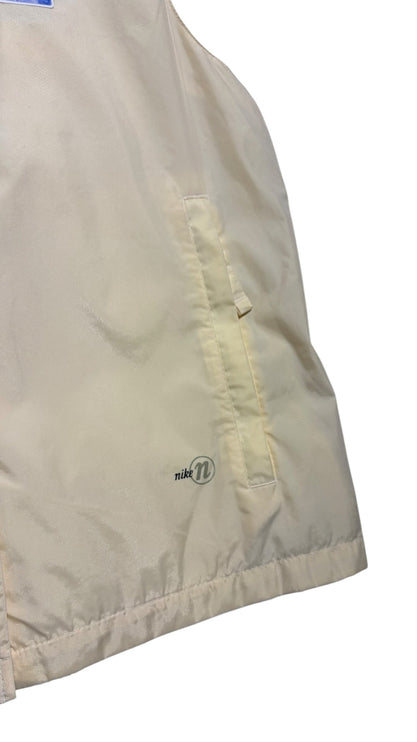 OutOf10 Nike sleeveless performance vest in cream synthetic fabric with a zippered side pocket and subtle logo detail.